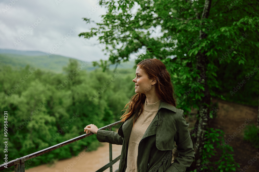 happy woman in a raincoat walks in the spring in the park near a stormy, mountain river happy woman in a raincoat walks in the spring in the park near a stormy, mountain river