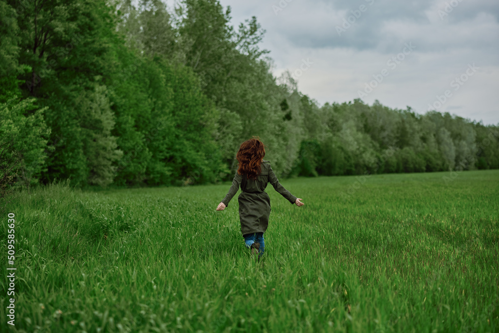 a woman in a long raincoat runs across a field in tall green grass in cloudy weather in spring a woman in a long raincoat runs across a field in tall green grass in cloudy weather in spring