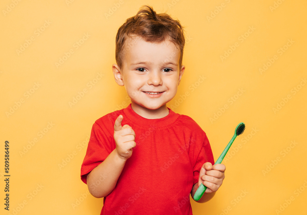 The happy kid is holding a toothbrush on a yellow background and smiling showing his teeth. Health care, oral hygiene The happy kid is holding a toothbrush on a yellow background and smiling showing his teeth. Health care, oral hygiene