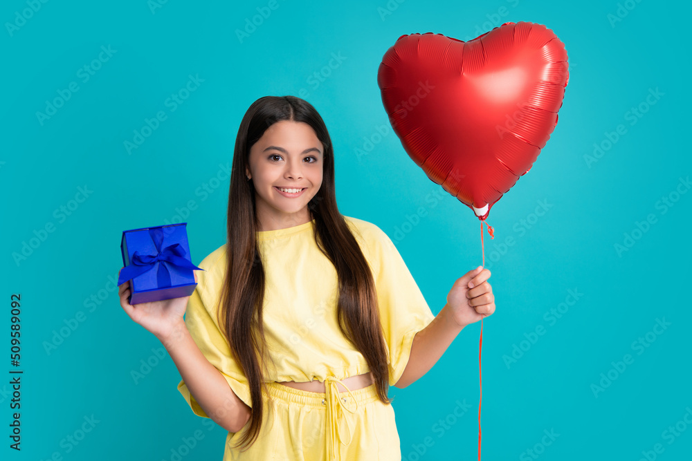 Teenager child holding gift box on blue isolated background. Gift for kids birthday. Christmas or New Year present box. Happy girl face, positive and smiling emotions. Teenager child holding gift box on blue isolated background. Gift for kids birthday. Christmas or New Year present box. Happy girl face, positive and smiling emotions.