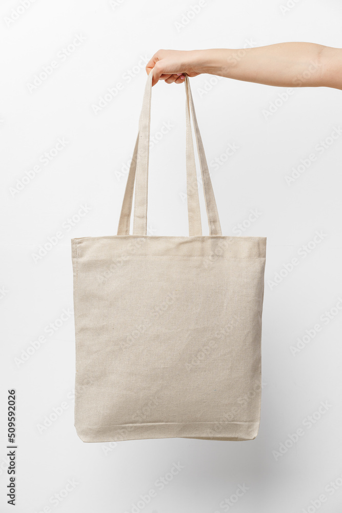 Female hand holding eco or reusable shopping bag against white background - obrazy, fototapety, plakaty 