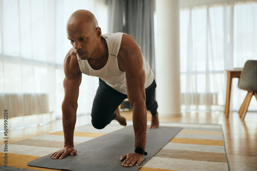 Fototapeta premium Young African American athletic man in plank pose doing running abs exercise during home workout.