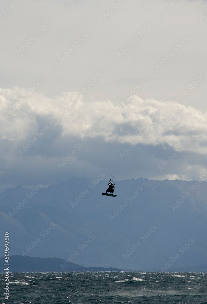 Fototapeta premium kitesurfing, sportsman jumping kitesurfing on a lake with mountains in the background