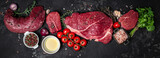 Set of fresh raw beef steak with spices ready to cook on a dark background. Long banner format. top view