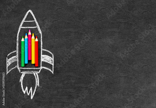A rocket is drawn on a school board with chalk, colored pencils are laid out