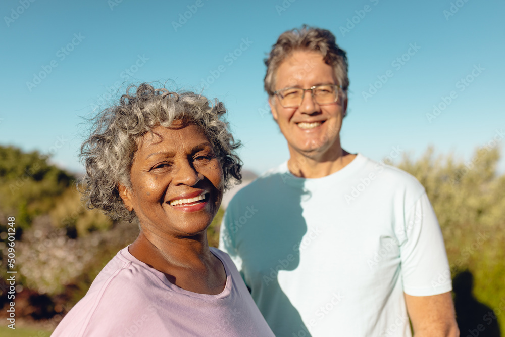 Portrait of smiling multiracial senior male and female friends standing against clear sky in yard