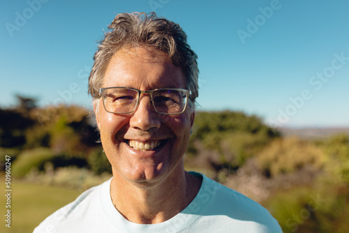Close-up portrait of smiling caucasian senior man wearing eyeglasses against clear blue sky in yard