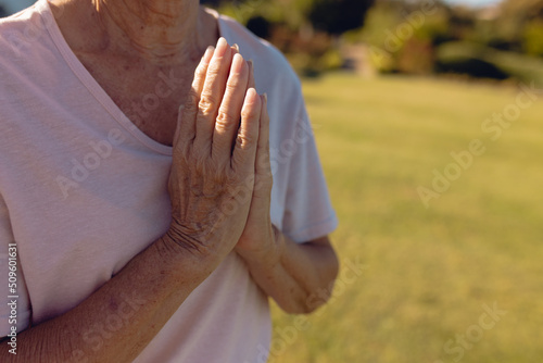 Midsection of asian senior woman meditating in prayer position in yard at retirement home