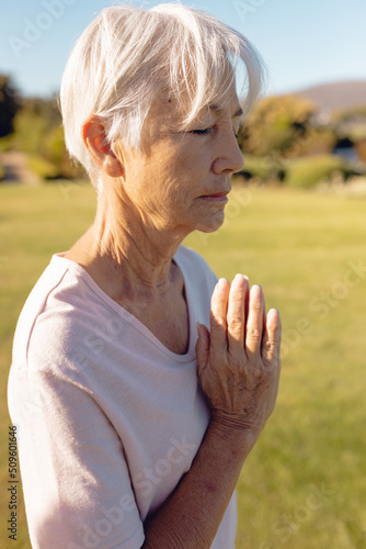 Asian senior woman with eyes closed meditating in prayer position in yard against clear sky
