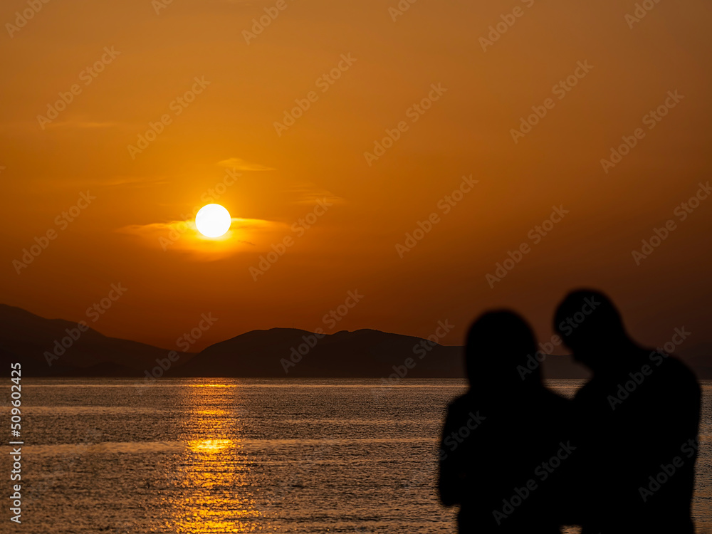A couple at a sea beach with colorful sunset sky. Panoramic beach landscape. Tropical beach and seascape and a distant island in the background. Calmness, tranquil, relaxing sunlight, summer mood. A couple at a sea beach with colorful sunset sky. Panoramic beach landscape. Tropical beach and seascape and a distant island in the background. Calmness, tranquil, relaxing sunlight, summer mood.