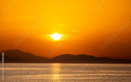 Panoramic beach landscape. Tropical beach and seascape and a distant island in the background. Orange and golden sunset sky, calmness, tranquil relaxing sunlight, summer mood. © Dimitrios