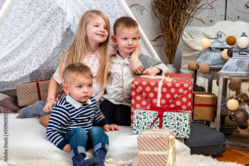 happy children sit between Christmas gift boxes and toys in a decorated house