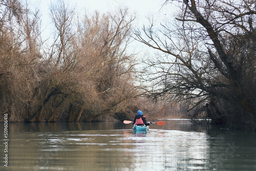 Rear view of woman kayaking on blue kayak in winter river near trees