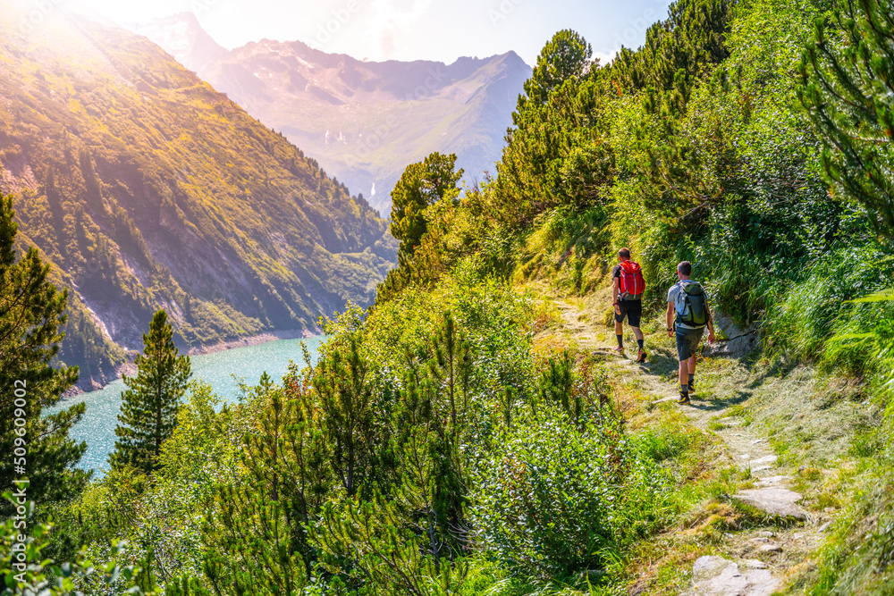 Fototapeta premium Alpine track and two hikers at mountain lake