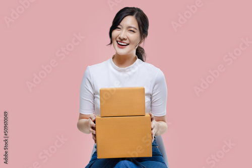 Happy Asian woman holding package parcel boxs isolated on pink screen background. Delivery courier and shipping service concept. © RedcupStudio