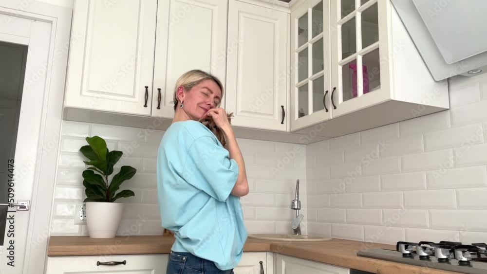 happy girl with short blond hair holds her little dog in her arms and cuddles with her at home in the kitchen, love and care for pets happy girl with short blond hair holds her little dog in her arms and cuddles with her at home in the kitchen, love and care for pets