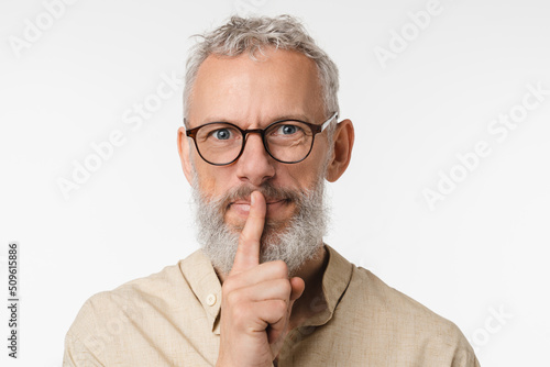 Top secret rumor gossip. Caucasian mature middle-aged man wearing glasses gesturing finger on lips for silence hush sound isolated in white background. photo