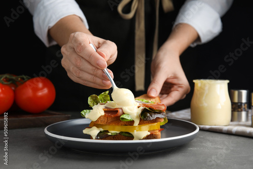 Woman making sandwich with mayonnaise at grey table, closeup photo
