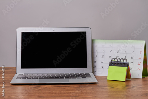 Laptop macbook with calendar and sticky notes on wooden desk. Notebook pc with black screen for copy space.