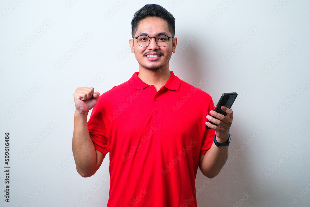 Young handsome man wearing casual shirt and glasses standing over isolated white background very happy and excited doing winner gesture with arms raised, smiliing while looking to camera Young handsome man wearing casual shirt and glasses standing over isolated white background very happy and excited doing winner gesture with arms raised, smiliing while looking to camera