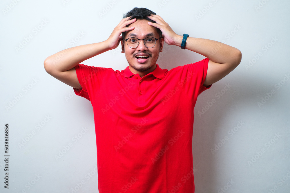 Fototapeta premium Portrait of a confused young handsome man wearing casual shirt and glasses with hands on his head