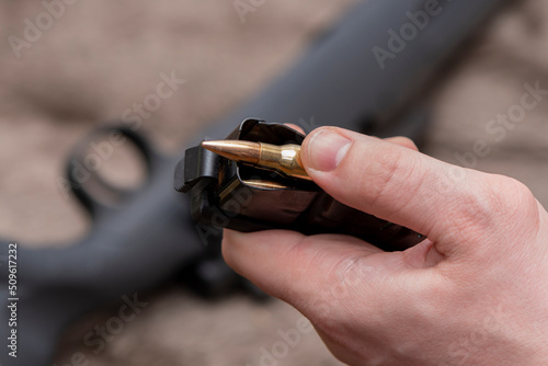 A male hunter loads cartridges for a rifle magazine on a blurry background, equips a combat weapon. photo