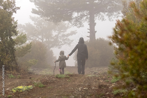 Mother daughter silhouette shot in foggy and hazy image on forest road in nature.