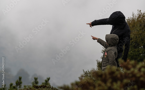 Selective focus shot of woman and child are pointing misty mountains together on a foggy day.