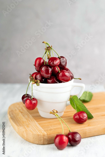 Ripe cherries in a white cup on a wooden board on a gray background.