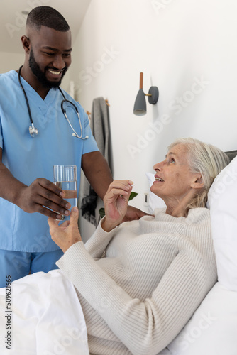 African american male health worker giving a glass of water to caucasian senior woman lying on bed © WavebreakMediaMicro