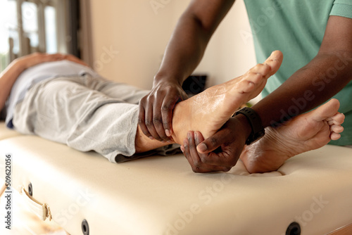 African american male physiotherapist giving foot massage therapy to caucasian senior woman at home