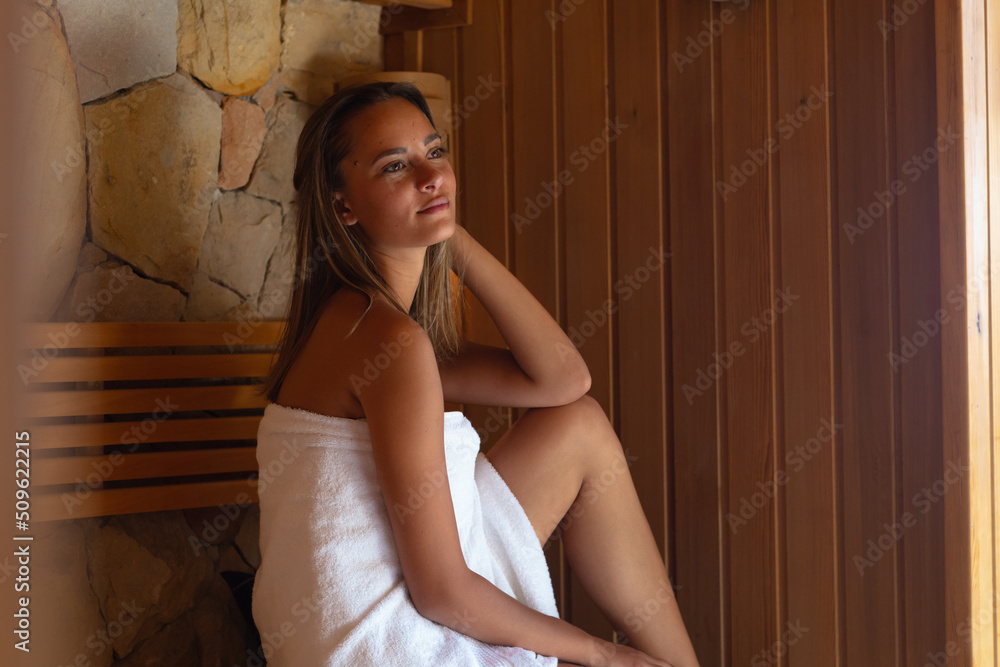Fototapeta premium Caucasian young woman in a bathrobe relaxing in the sauna