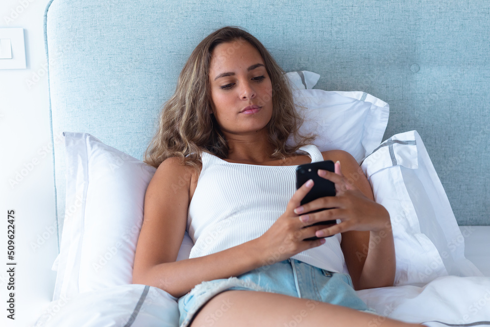 Caucasian young woman using smartphone lying on the bed at home Caucasian young woman using smartphone lying on the bed at home