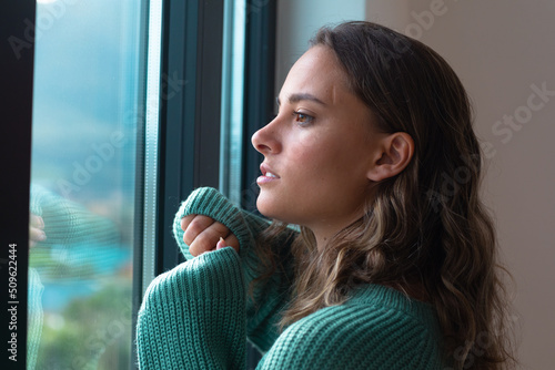 Caucasian beautiful young woman looking out of the window at home