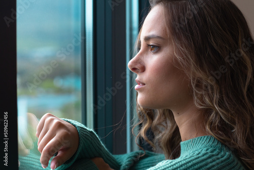 Close up of caucasian young woman looking out of the window at home