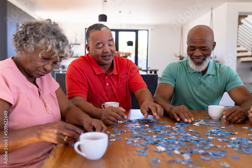 Multiracial senior friends arranging jigsaw pieces on table while enjoying coffee in nursing home