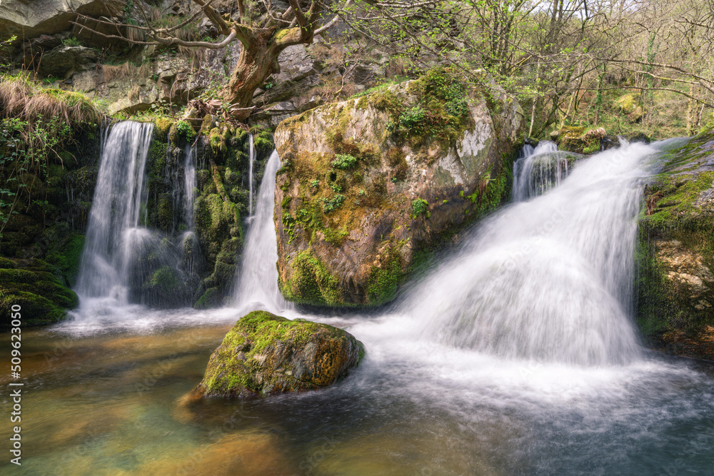 Fototapeta premium Waterfalls over a mossy dam and limestone blocks in a small river