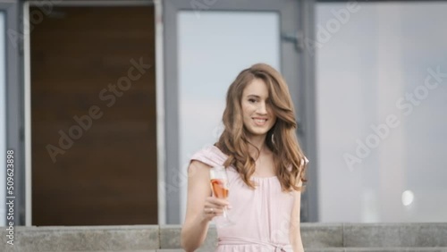 Beautiful brunette Caucasian appearance in a pink dress with a glass of champagne posing in front of the camera at a party