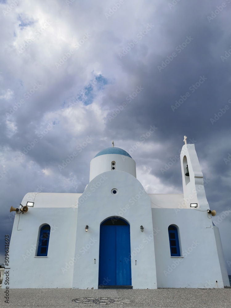 The Church of St. Nicholas the Wonderworker is white with a blue door against the backdrop of  the dramatic sky.