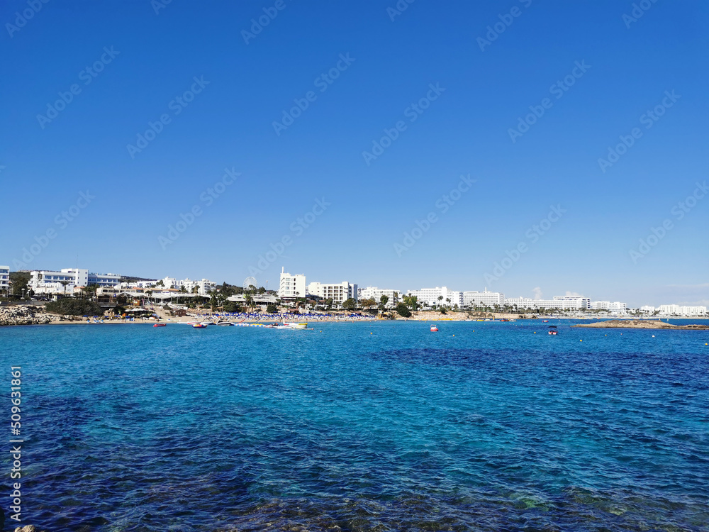 View of the sandy beach of Fig Tree Bay, the city and the island against a blue sky with clouds.