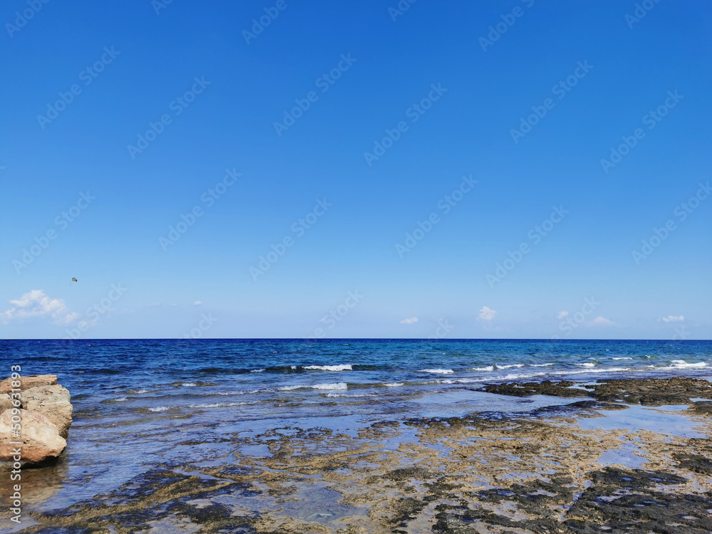 The coast of the Mediterranean Sea, waves, clear water, a stone ridge against a blue sky with clouds. The coast of the Mediterranean Sea, waves, clear water, a stone ridge against a blue sky with clouds.