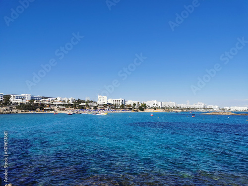 View of the sandy beach of Fig Tree Bay, the city and the island against a blue sky with clouds.