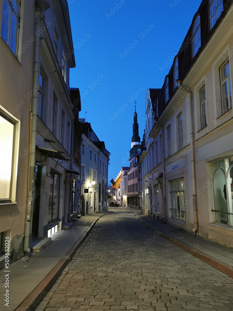 A narrow cobbled street in the Old City, at the end of which you can see the spire of the Church of the Holy Spirit against the blue sky. Old Tallinn.