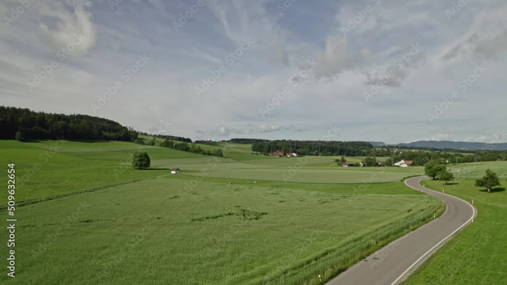 Agricultural field and meadow with country road between and passing cars at Village of Forch on a blue cloudy summer day. Movie shot June 8th, 2022, Zurich, Switzerland. Agricultural field and meadow with country road between and passing cars at Village of Forch on a blue cloudy summer day. Movie shot June 8th, 2022, Zurich, Switzerland.