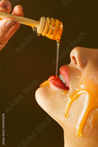 Honey dripping from honey dipper on sexy girl lips. Thick honey dipping from the wooden honey spoon. Beauty model woman open mouth, model eating nectar. Healthy food concept, diet, dessert.