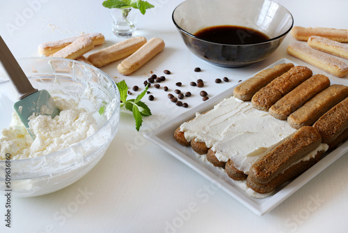 Preparare il tiramisù italiano con savoiardi, mascarpone, caffè espresso su tavola bianca. photo