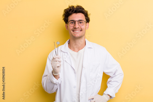 young handsome guy smiling happily with a hand on hip and confident. dentist concept