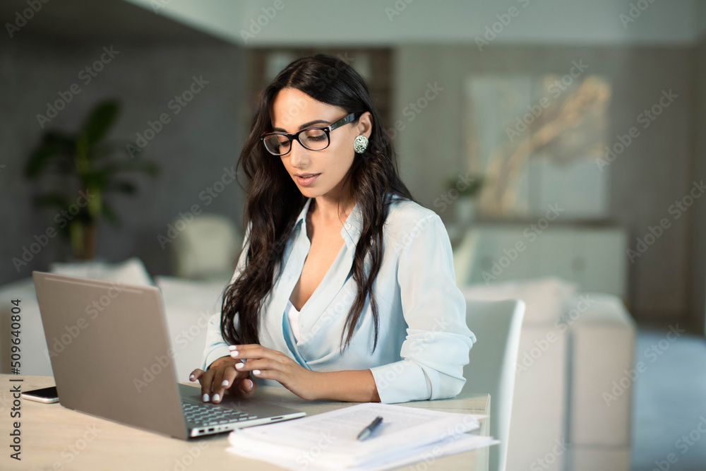Smiling successful female in eyeglasses using laptop computer indoors at home office, making notes on papers, remote work and small business freelancer, education and student,self employed Smiling successful female in eyeglasses using laptop computer indoors at home office, making notes on papers, remote work and small business freelancer, education and student,self employed