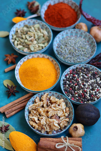 Close up photo of spices and herbs in blue ceramic bowls. Paprika, turmeric, anise, lavender, cardamom, cinnamon, pepper on textured blue background. 