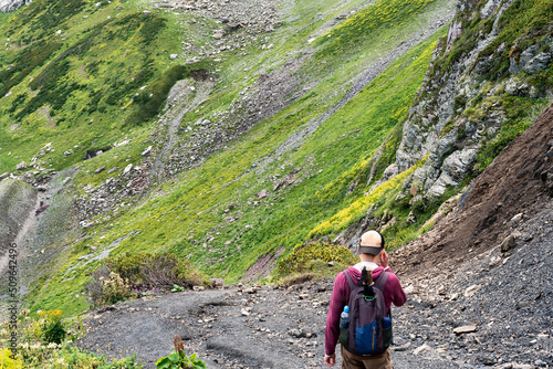 rear view of Young man in cap with backpack hiking in mountains in summer healthy active lifestyle, outdoor activities, landscape selective focus soft focus defocused